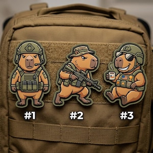 May include: Three cartoon capybara patches on a tan backpack. Each capybara is dressed in military gear. One wears a headset, another holds a rifle, and the third wears sunglasses and holds a mug. Each patch is numbered.