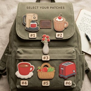 May include: An olive green canvas backpack featuring the text SELECT YOUR PATCHES and six numbered silicone patches: a coffee maker, a mug with a cherry, a vase of flowers, a red mug, a picnic basket, and a red toaster.