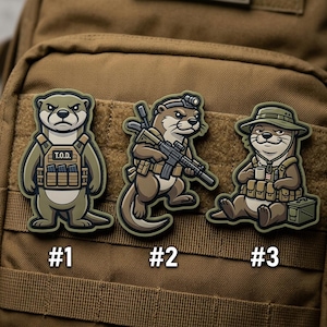 May include: Three tactical patches featuring cartoon otters. One otter wears a vest with the text "T.O.D.", another holds a rifle, and the third is seated with a cup and hat. Each patch is numbered.