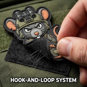 May include: A rubberized morale patch featuring a cartoon mouse wearing a tactical helmet with night vision goggles. The patch has a black hook-and-loop system backing, allowing it to be attached to fabric surfaces. The design is detailed and colorful.