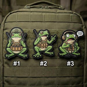 May include: Three green frog patches with black borders. Each frog is depicted in a military-style outfit, holding a weapon or wearing a headset. The patches are numbered #1, #2, and #3. One patch has a speech bubble that says "ROGER THAT".