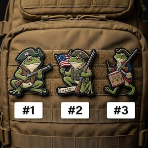 May include: Three patches featuring cartoon frogs in Revolutionary War attire. Each frog is depicted with a tricorn hat and holding a weapon or drum. The patches are numbered #1, #2, and #3, and are set against a brown background.