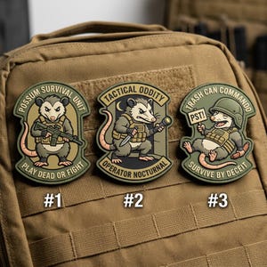 May include: Three tactical patches featuring cartoon opossums in military gear. The patches have text that reads "Possum Survival Unit", "Tactical Oddity", and "Trash Can Commando". Each patch has a unique design and slogan.