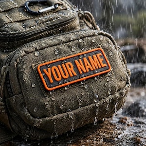 May include: An olive green tactical pouch featuring a rectangular patch with the orange text YOUR NAME. The textured fabric is covered in water droplets, and a black carabiner is attached to the top section of the gear bag.