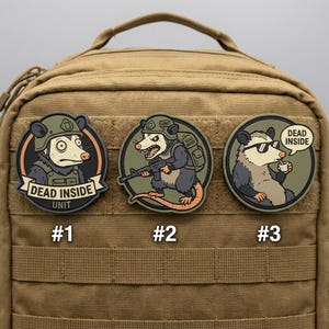 May include: Three round patches featuring cartoon opossums with the text "DEAD INSIDE." One opossum wears a helmet, another holds a rifle, and the third wears sunglasses and sips from a cup. The patches are on a tan backpack.