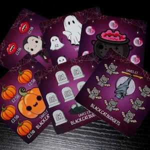 May include: A collection of five square Halloween-themed savings challenge cards with a purple background and spiderweb patterns. The cards feature cartoon illustrations of pumpkins, a ghost, a vampire, a cauldron, tombstones, and bats with text.