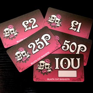 May include: A set of five rectangular cards with a pink and black gradient background. Each card features a graphic of two skulls surrounded by pink roses and the text BLACK.CAT.BUDGETS. The cards display the denominations £2, £1, 25P, 50P, and IOU.