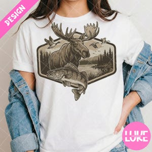 Puede incluir: Camiseta blanca con un diseño de temática natural. El diseño incluye un alce, un pez, patos y una escena de lago dentro de un marco hexagonal. La camiseta tiene una etiqueta rosa "DESIGN" y una etiqueta rosa "LUKE".