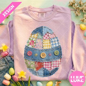 Può includere: Felpa rosa chiaro con un design a patchwork a forma di uovo di Pasqua. L'uovo è realizzato con vari modelli di tessuto, tra cui floreale, gingham e denim. Ha una fascia in denim con tre bottoni e stelle ricamate. La parola "DESIGN" è in uno striscione rosa.