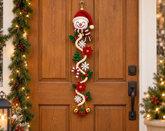 May include: A vertical crochet wall hanging featuring a smiling snowman head wearing a red hat and striped scarf. The piece includes a winding cream-colored rope adorned with red poinsettias, green holly leaves, white snowflakes, a tree, and candy canes.