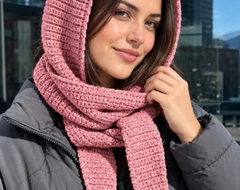 May include: A dusty pink knitted hooded scarf featuring a ribbed texture and long, tapered ends. The accessory is worn over a dark gray puffer jacket, providing full head and neck coverage with its integrated hood and wrap-around design.