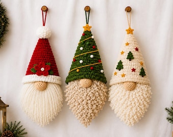 May include: Three hanging crochet gnome ornaments with long beards. The left gnome wears a red hat with a white pom-pom and a red flower. The center gnome has a green hat with small colorful pom-poms. The right gnome has a cream hat with small tree and star appliques.