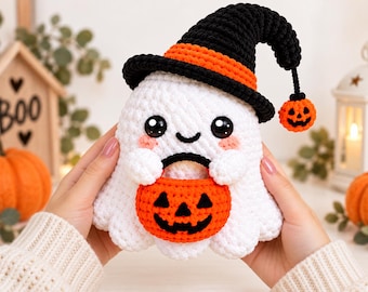 May include: A white crocheted ghost plush toy wearing a black witch hat with an orange band and a dangling orange jack-o'-lantern charm. The ghost has large black eyes, a small smile, pink cheeks, and holds a small orange jack-o'-lantern bucket.