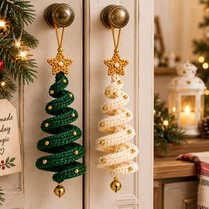 May include: Two spiral-shaped crochet Christmas tree ornaments, one dark green and one cream, each topped with a crocheted star and a small pearl. Both trees are decorated with gold beads and feature a gold jingle bell at the bottom point.