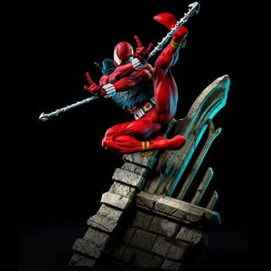 May include: A red and black Spider-Man action figure in a dynamic pose, perched on a stone structure against a black background. The figure is detailed with white accents, yellow bands, and a web-like design on the chest.