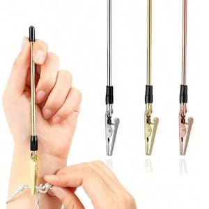 Puede incluir: Un conjunto de cuatro clips metálicos para joyería en tonos plateado, dorado y oro rosa. Cada clip tiene una varilla con punta negra y una pinza articulada. Un clip está sujeto a una pulsera.