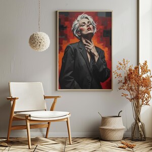 Könnte beinhalten: Ein gerahmter Kunstdruck mit einem Porträt einer Person in einem schwarzen Blazer mit weißem Haar und rotem Lippenstift. Der Hintergrund ist eine Mischung aus roten und orangen Farbtönen. Das Kunstwerk wird in einem Raum mit einem Stuhl und dekorativen Elementen ausgestellt.