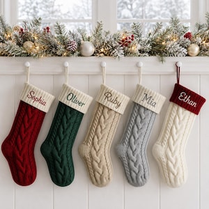 May include: Five cable-knit Christmas stockings hanging in a row. From left to right, the stockings are red with the name Sophia, dark green with Oliver, beige with Ruby, gray with Mia, and white with Ethan embroidered on the cuffs.