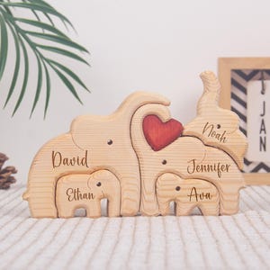 May include: Wooden elephant family puzzle with the names "David", "Ethan", "Noah", "Jennifer", and "Ava" engraved on the pieces. A red heart is in the center. The puzzle is made of light-colored wood.