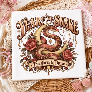 Könnte beinhalten: Ein quadratischer weißer Leinwanddruck mit einer gewundenen Schlange, einer Mondsichel und roten Rosen. Der Text lautet "YEAR OF THE SNAKE" oben und "Transform & Thrive" auf einem Banner unten. Das Design enthält Sternakzente und hängende Mondanhänger.