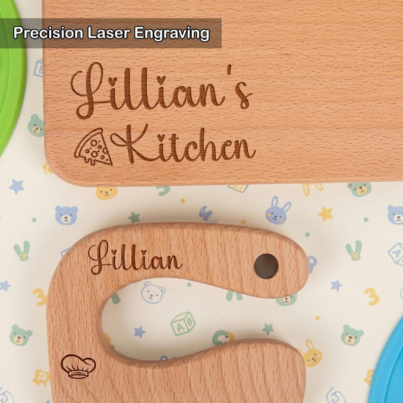 Close-up of precision laser engraving on a custom kids kitchen tool set. The wooden cutting board reads Lillian's Kitchen with a pizza slice, and the toddler knife is engraved with Lillian and a chef hat. High-quality personalized Montessori gift.
