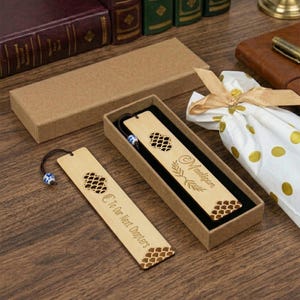 Op de afbeelding: Houten bladwijzers met lasergesneden patronen en de opschriften "Madison" en "To Our Next Chapters". De bladwijzers worden gepresenteerd in een geschenkdoos, met een decoratieve kraal aan het touwtje. Het kleurenschema is in natuurlijke houttinten.