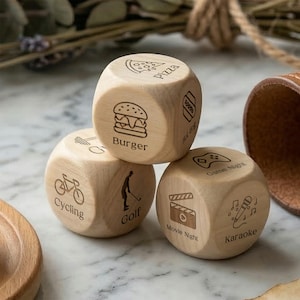 May include: Three wooden dice with engraved icons and text. One die shows a burger, pizza, and hot dog. Another die shows cycling and golf. The third die shows movie night, karaoke, and game night.