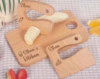 May include: Wooden toy kitchen set with a cutting board, two cleavers, and a banana. The cleavers and cutting board are engraved with the name "Ethan" and "Ethan's Kitchen". The set includes a carrot and cake illustration.