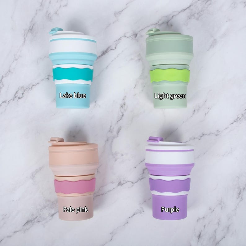 A clean, top-down flat lay view displaying the four color options for the personalized collapsible silicone water cups on a marble surface. The set includes Lake Blue, Light Green, Pale Pink, and Purple, each featuring a silicone bottle band.