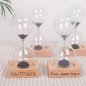 Peut inclure: Plusieurs sabliers en verre transparent avec du sable noir, posés sur des socles en bois. L'un est gravé "Mia ♥ Jack", l'autre "A new chapter begins". Ces sabliers sont décoratifs et peuvent servir à mesurer le temps.