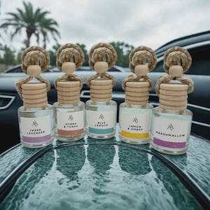 May include: Five car air fresheners with wooden tops and rope detailing. Each glass bottle has a label with the initials "AB" and a scent name: Fresh Lavender, Myrrh & Tonka, Blue Lagoon, Lemon & Amber, and Marshmallow.