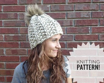 Op de afbeelding: Een gebreide muts met een pluche pompon in crème en bruin met de tekst "KNITTING PATTERN!" in een roze ster.