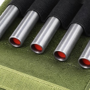 Puede incluir: Primer plano de cinco tubos metálicos plateados con interiores rojos, sujetos por correas de tela negra. Los tubos están sobre un fondo de tela verde, lo que sugiere un estuche de almacenamiento.