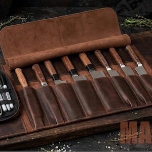 Puede incluir: Un estuche de cuero marrón para cuchillos con múltiples ranuras para cuchillos de cocina, con un compartimento lateral dedicado que contiene un rallador pequeño, un pelador, unas pinzas de metal y tres marcadores. Se asegura con correas de cuero.