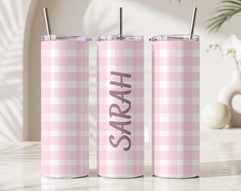 May include: Three cylindrical stainless steel tumblers with a light pink and white gingham check pattern. Each tumbler features a clear lid and a thin metal straw. The center tumbler displays the name SARAH in a dark pink vertical script font.