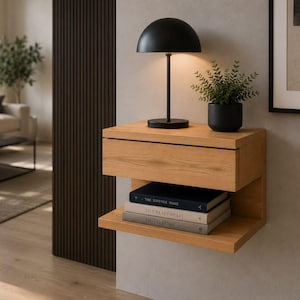 May include: A wall-mounted light oak floating nightstand featuring a single drawer and an open lower shelf. A black dome-shaped table lamp and a small potted green plant sit on top, with three stacked books resting on the lower shelf.