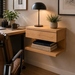 May include: A wall-mounted light oak floating nightstand featuring a single horizontal drawer and an open storage shelf below. The shelf holds three stacked books titled The Kinfolk Home, Live Beautifully, and This is Home.