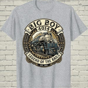 May include: A heather gray t-shirt featuring a circular graphic of a steam locomotive. The text reads BIG BOY 4014 LEGEND OF THE RAILS EST. 1941. The design includes a train on tracks, smoke, and gear-like borders in shades of cream, black, and tan.