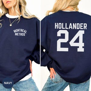 May include: Navy blue sweatshirt with white text. The front displays "MONTREAL METROS" above the chest. The back features "HOLLANDER" and the number "24" in white. The bottom left corner shows the word "NAVY".