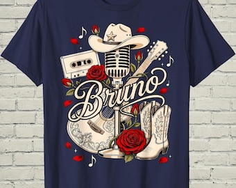 May include: A navy blue t-shirt featuring a graphic print of a vintage microphone, a cowboy hat, a guitar, a cassette tape, and cowboy boots. The design includes red roses, musical notes, and the name Bruno written in a cursive script font.