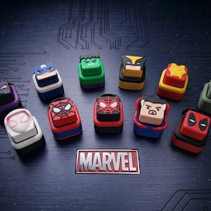 Może przedstawiać: Kolekcja jedenastu niestandardowych nakładek na klawisze klawiatury mechanicznej z różnymi wzorami postaci Marvela, w tym Spider-Manem, Iron Manem, Wolverinem i Hulkiem, ułożonych wokół centralnej prostokątnej tabliczki z logo Marvel na ciemnej powierzchni płytki drukowanej.