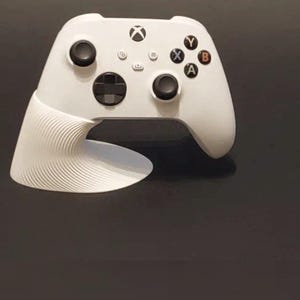 Op de afbeelding: Een witte Xbox-controller met een uniek, gebogen ontwerp aan de onderkant. De controller heeft zwarte knoppen en gekleurde actieknoppen (X, Y, A, B). Het ontwerp bevat een getextureerde, golfachtige grip voor verbeterde ergonomie.