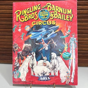 May include: Vintage Ringling Bros. and Barnum & Bailey Circus souvenir magazine cover. The red cover features circus performers, polar bears, and a spaceship. Text includes "The Greatest Show on Earth."