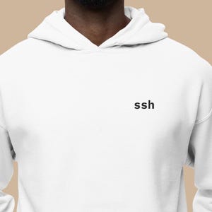 May include: White hooded sweatshirt with a front pocket and the word "ssh" printed in black on the chest. The sweatshirt is made of a soft material and has a drawstring hood.