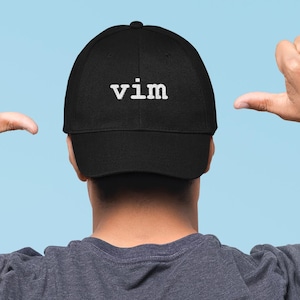 May include: A black baseball cap featuring the word vim embroidered in white lowercase letters on the front panel. The cap has a structured crown and a curved brim, constructed from a solid black fabric material with visible stitching details.