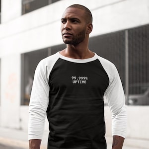 May include: A black and white baseball-style shirt with the text "99.999% UPTIME" in white. The shirt has a black body and white sleeves. The person is wearing blue jeans.