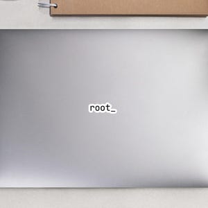 May include: A laptop with a sticker that reads "root_". A white computer mouse, a spiral-bound notebook, a pencil, a pair of black glasses, and two small potted plants are also visible.