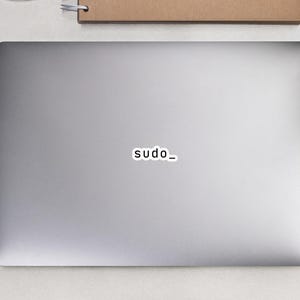 May include: A laptop with a sticker that reads "sudo_" in a sans-serif font. A white computer mouse, a spiral-bound notebook, a pencil, a pair of black glasses, and two small potted succulents are also visible.