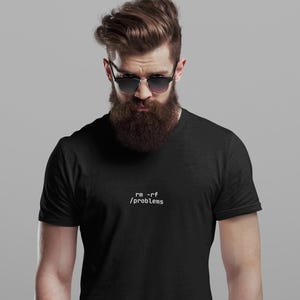 May include: Black t-shirt with the text "rm -rf /problems" in white. The shirt is a crew neck style. The person in the image is wearing sunglasses and has a full beard.