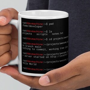 May include: A white ceramic mug featuring a black graphic print of a computer terminal command line interface. The text displays directory paths, file listings, and git status messages in white and red font against a solid black background.